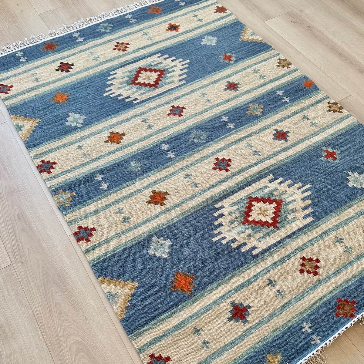 Covor Kilim Bimala, tesut plat in mod traditional din lana, model in romburi in nuante de bej si albastru, pe podea