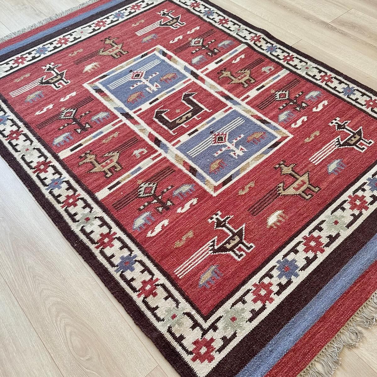 Covor traditional cu tesatura plata kilim Birdsong, multicolor cu modele aztece si simboluri native, nuante calde de rosu teracota, pe podea