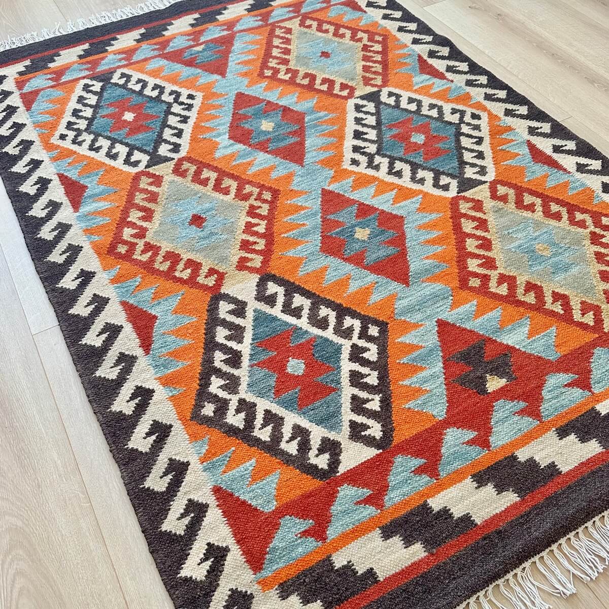 Covor traditional Kilim cu tesatura plata Saira, model mic 120x180, multicolor nuante calde de rosu portocaliu crem cu modele geometrice in romb, pe podea