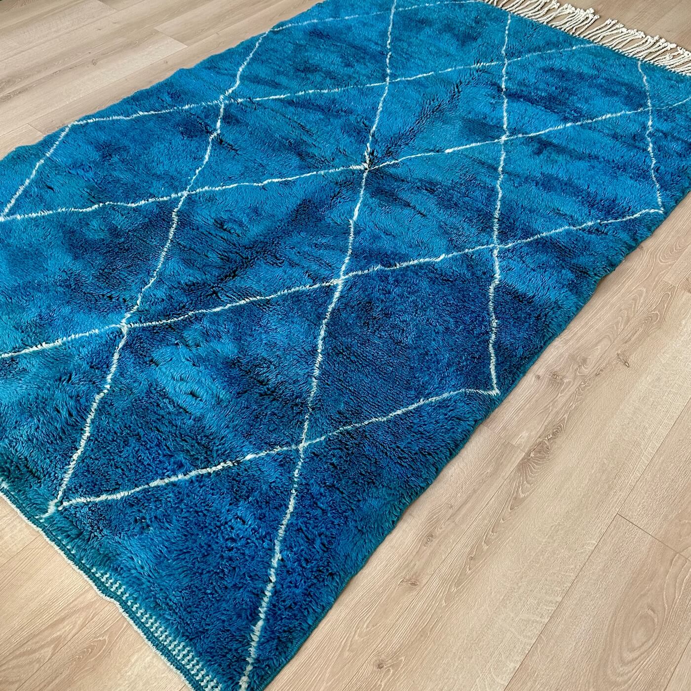Covor gros și pufos din lână naturală realizat manual în Mrirt, Maroc. Perfect pentru living sau dormitor - dimensiune mare cu linii asimetrice albe pe un fundal albastru turcoaz - întins pe parchet