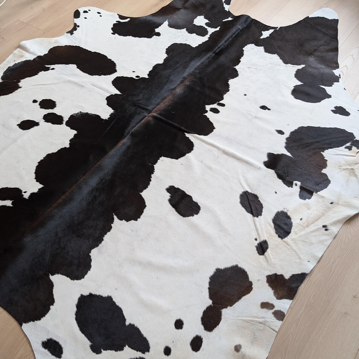 covor din piele de vaca naturala in culori negru cu alb cu pete pe parchet, mango+bloom