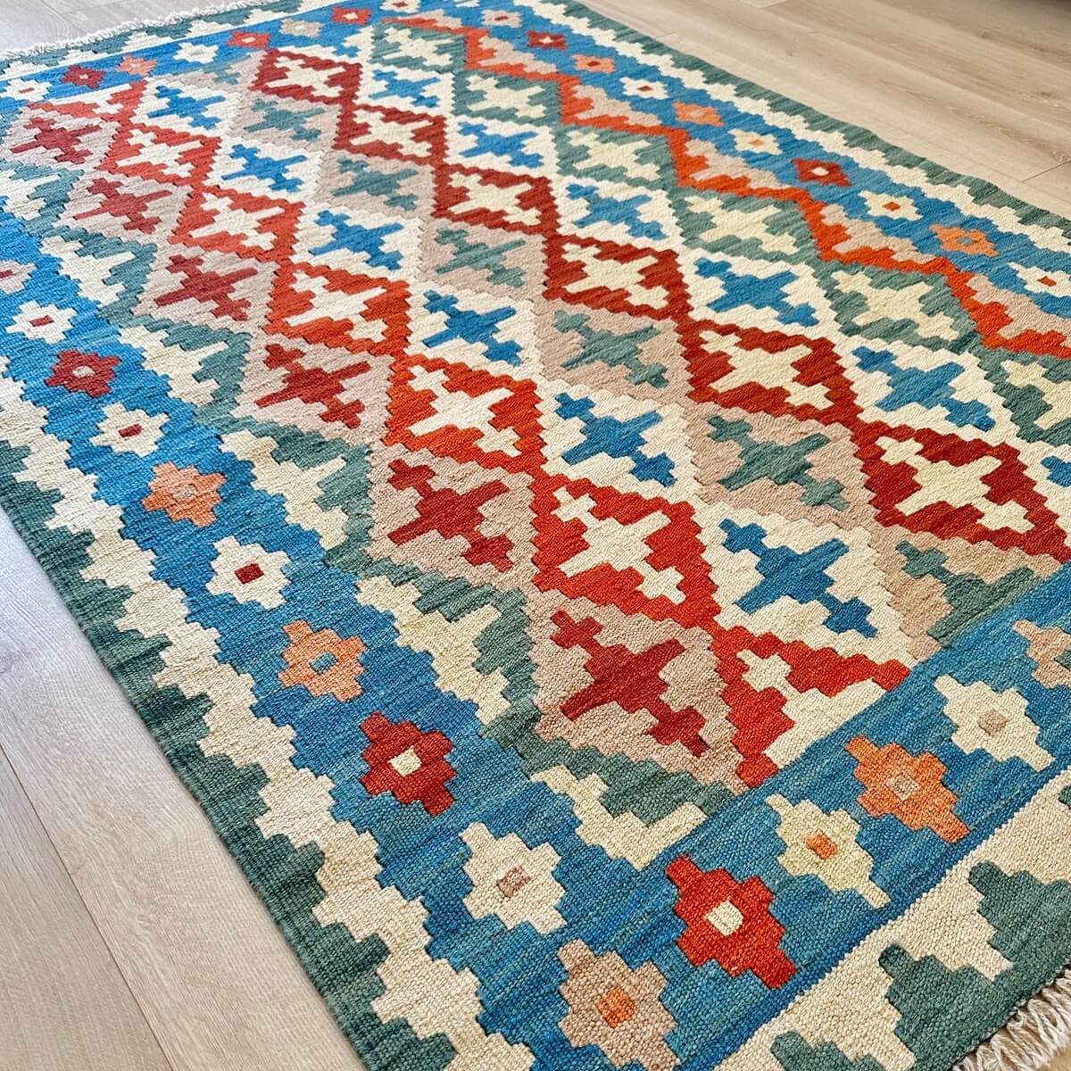 Covor traditional Kilim tesut plat - subtire si durabil - tesut plat din lana in Iran - multicolor in nuante de verde albastru rosu pe fundal crem, pe podea