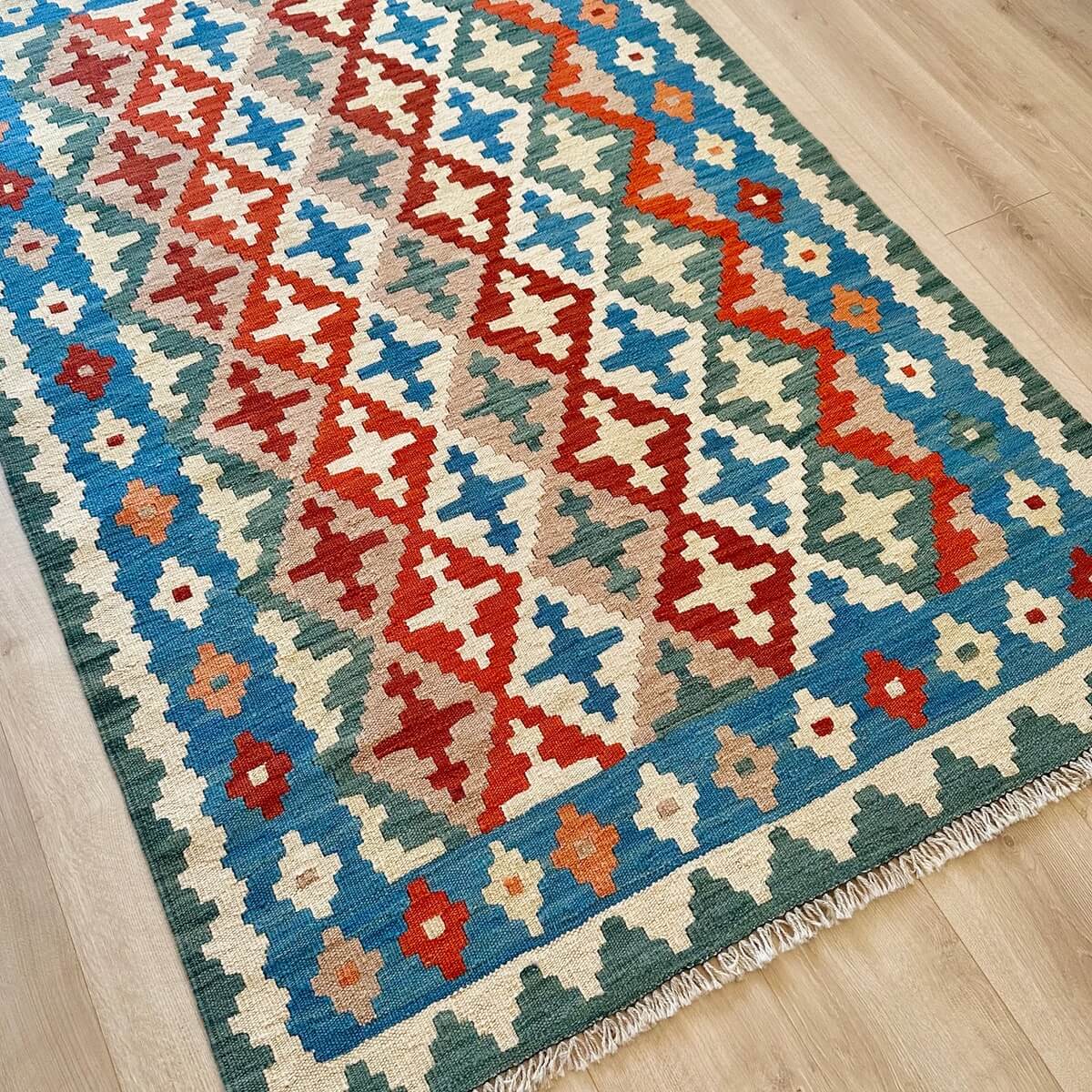 Covor traditional Kilim tesut plat - subtire si durabil - tesut plat din lana in Iran - multicolor in nuante de verde albastru rosu pe fundal crem, pe podea 2