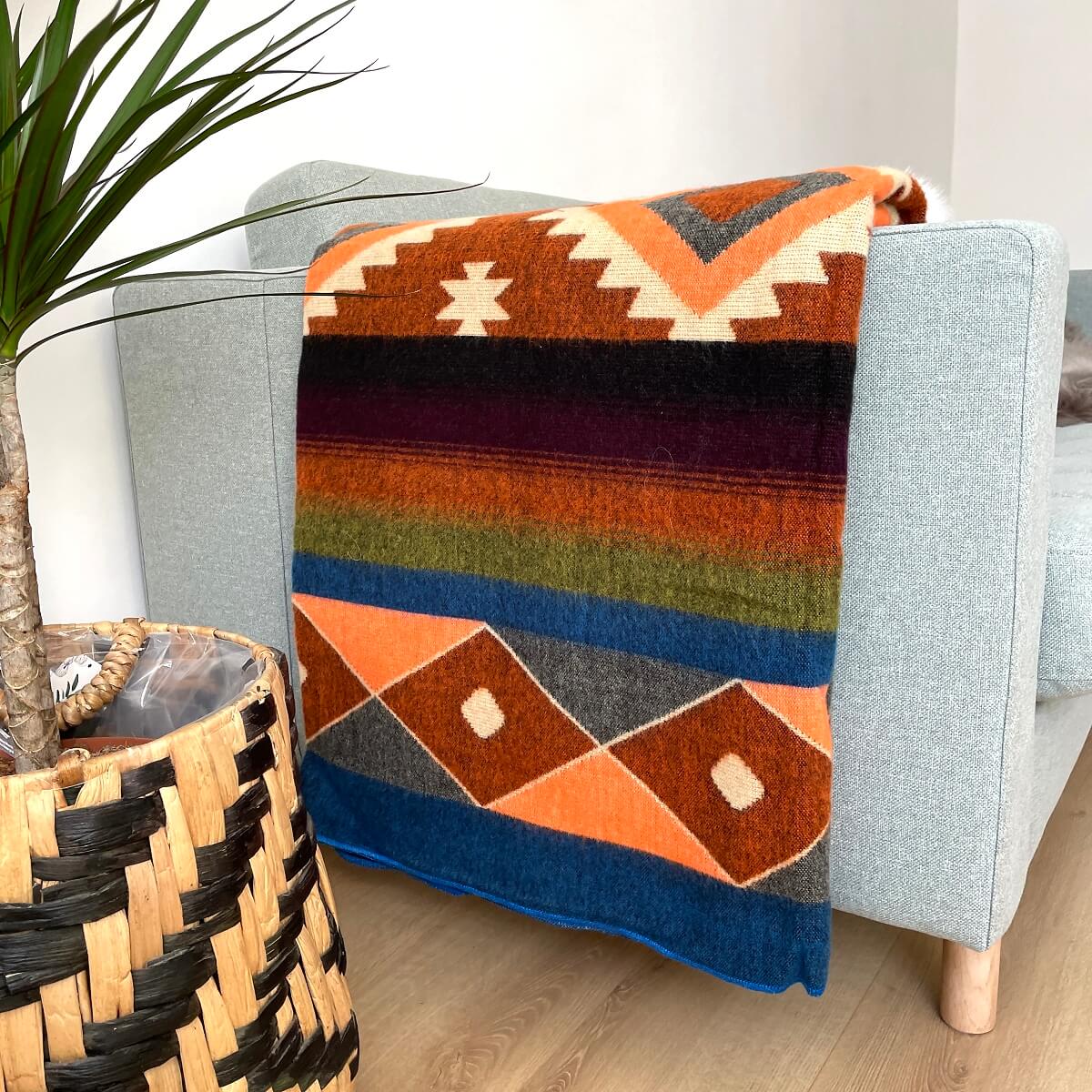 patura din lana de alpaca cu forme aztece in nuante multicolore quilotoa albastru pe canapea