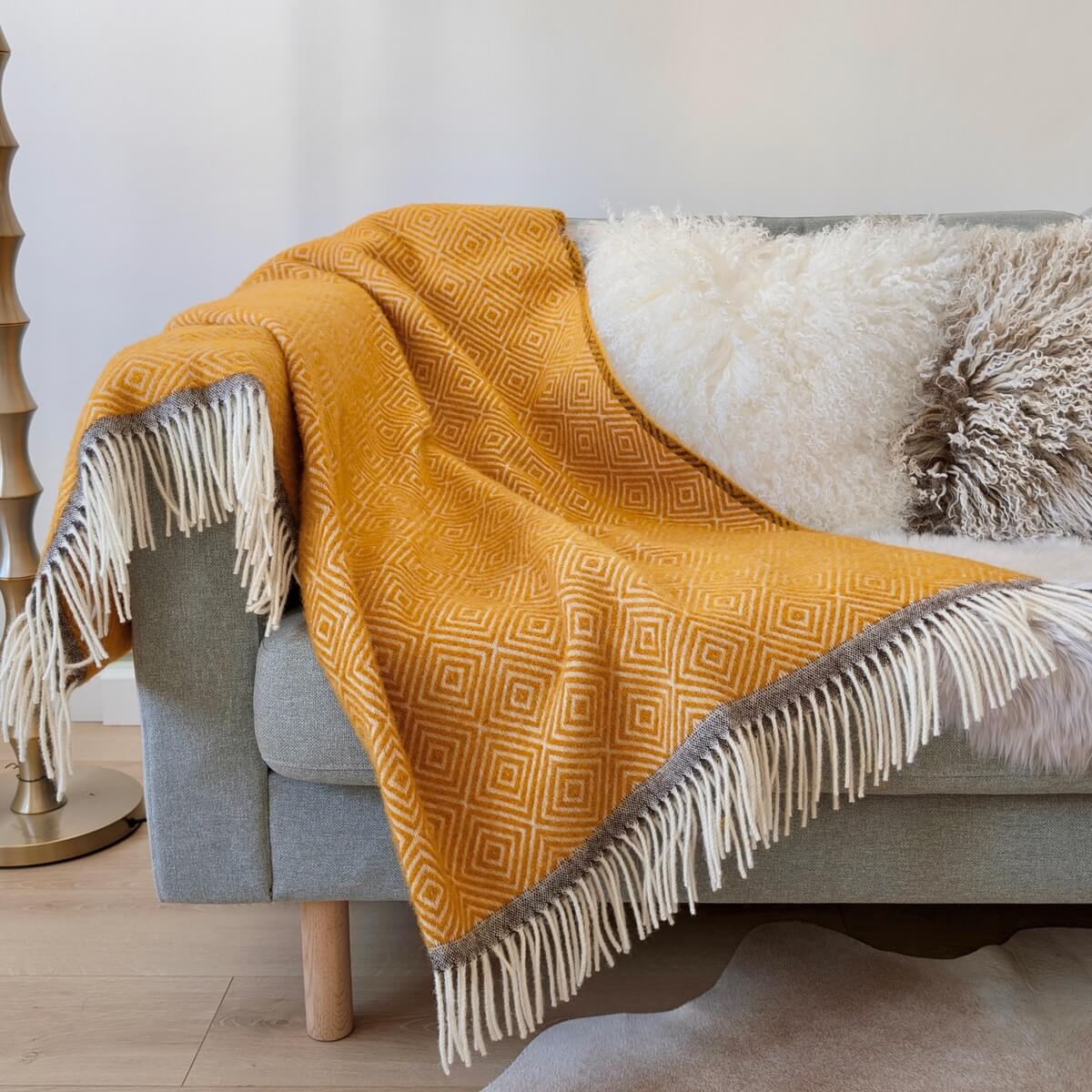 Patura groasa Venezia realizata 100% din lana de Noua Zeelanda, design modern cu romburi albe si ciucuri pe ambele parti, pe canapea