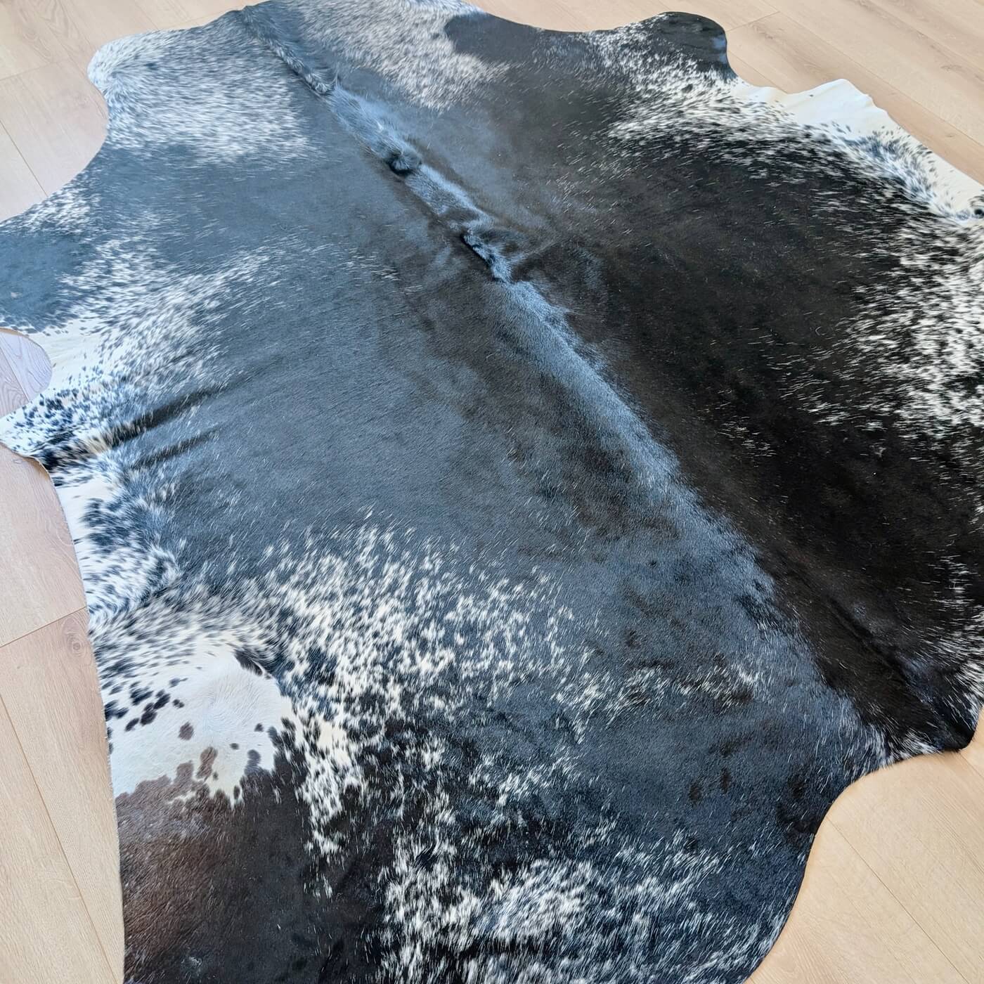 covor din piele de vaca pestrit cu fundal negru si detalii albe si gri - perfect pentru living, studio sau birou - intins