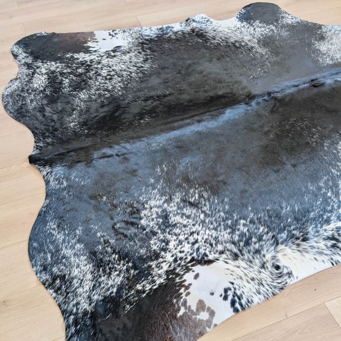 covor din piele de vaca pestrit cu fundal negru si detalii albe si gri - perfect pentru living, studio sau birou - pe parchet