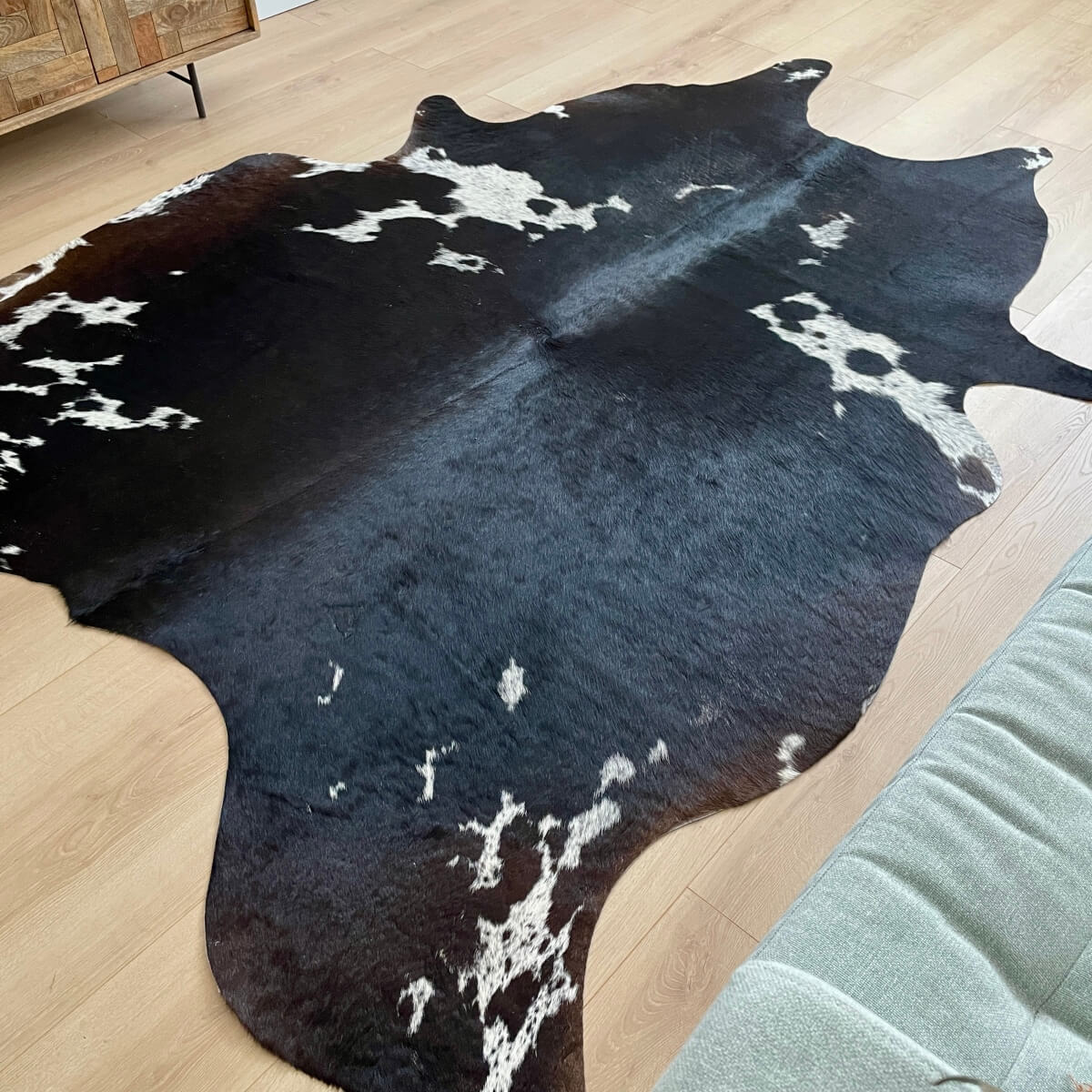 covor din piele de vaca neagra cu pete albe in fata canapelei, mango+bloom