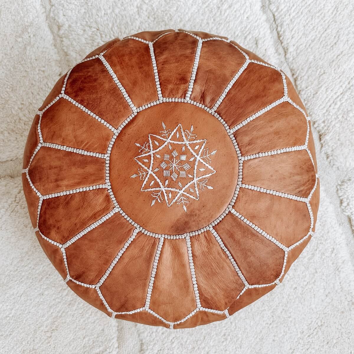 pouf marocan din piele naturala cusut manual de culoare maro deschis, pe covor